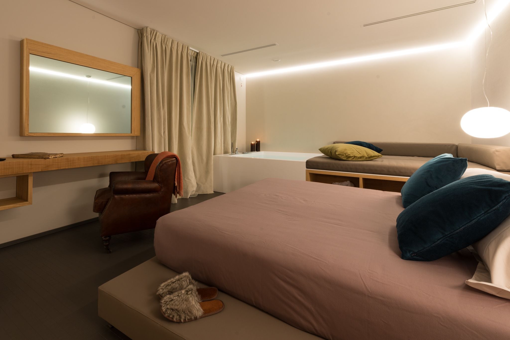 A modern hotel room with a large bed, a sofa, a chair, a vanity with a mirror, and a small table.