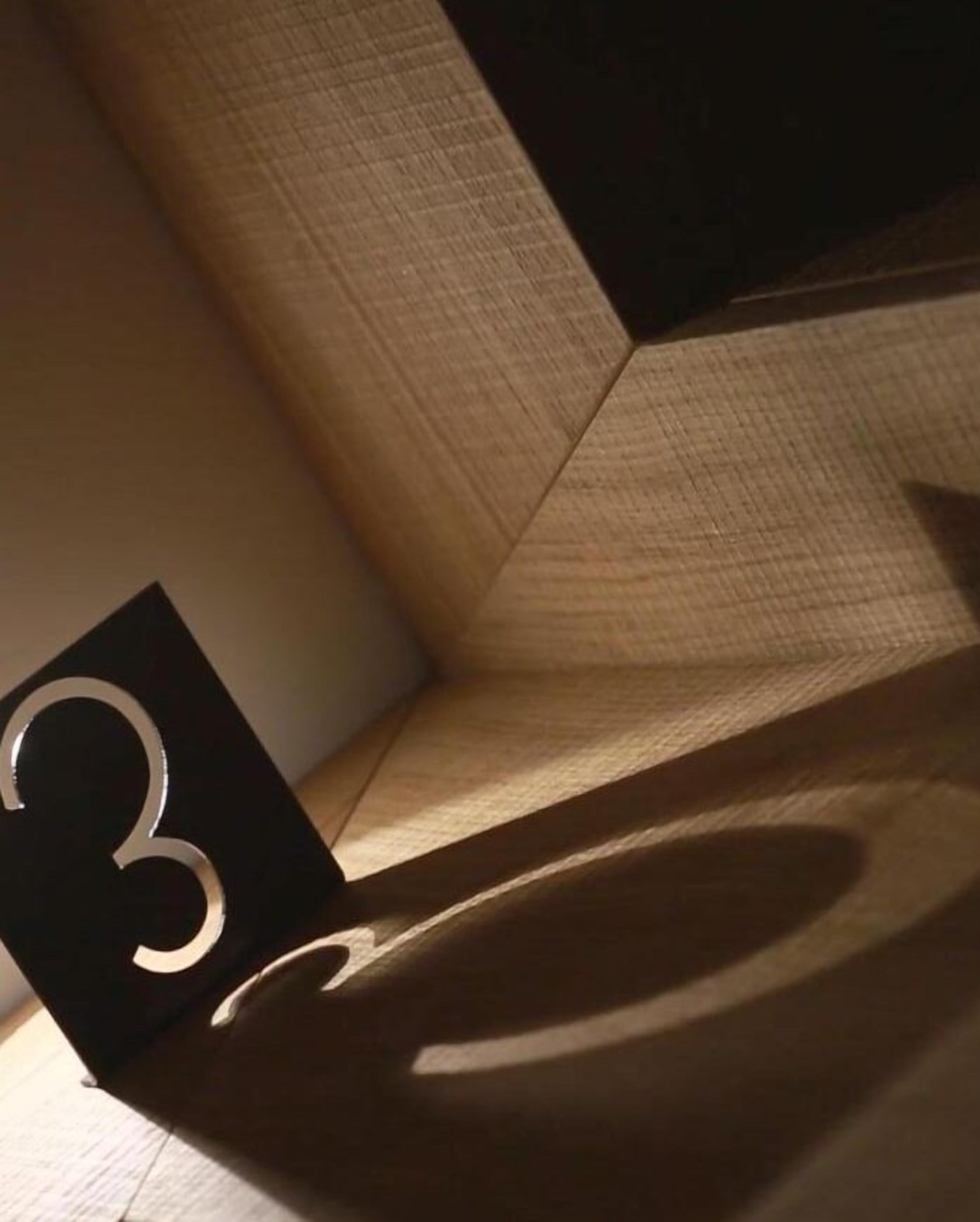 A corner of a room with a wooden floor and a black sign with the number 3.