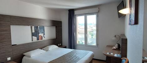 Une chambre d’hôtel avec un grand lit, un bureau, une chaise, une fenêtre avec des rideaux et un téléviseur fixé au mur.