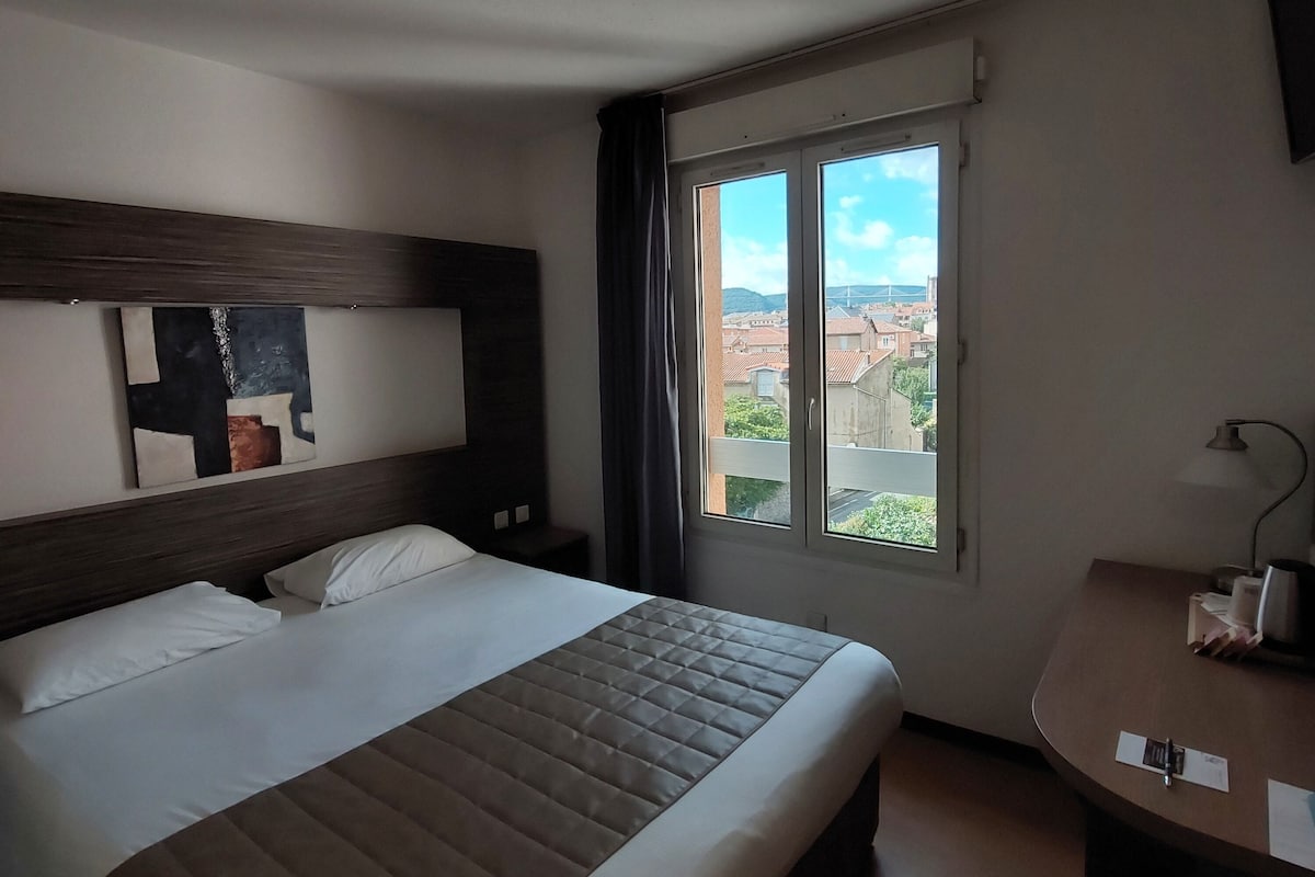 Habitación de hotel con una cama grande, un escritorio y una ventana con vista a la ciudad.