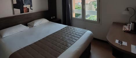 A hotel room with a large bed, a desk, and a window with a city view.