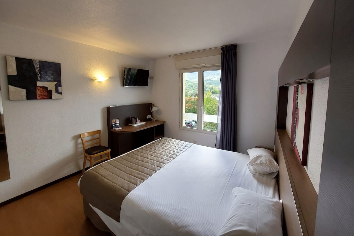 Habitación de hotel con cama, escritorio, silla, televisor y ventana con vistas.