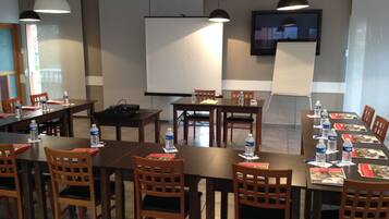 A conference room with long tables, chairs, water bottles, and a projector screen.