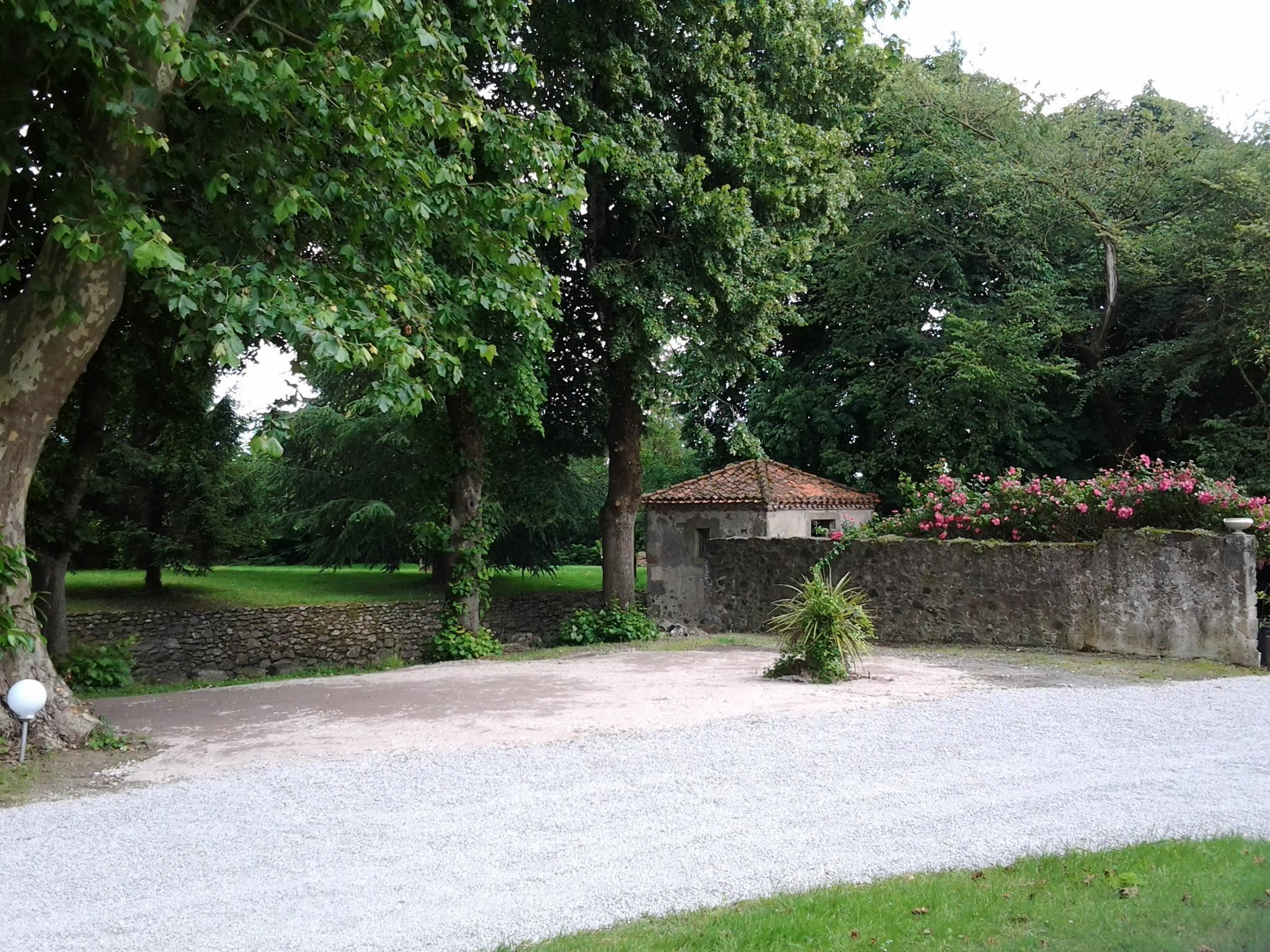 Ein Kiesweg führt zu einem kleinen Steinhaus mit Ziegeldach, umgeben von üppigem Grün und einer Steinmauer mit blühenden Pflanzen.