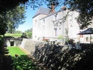 A stone wall, a grassy area, and a building with a tiled roof. - Le Manoir Aux Douves (Bazoges-en-Paillers)