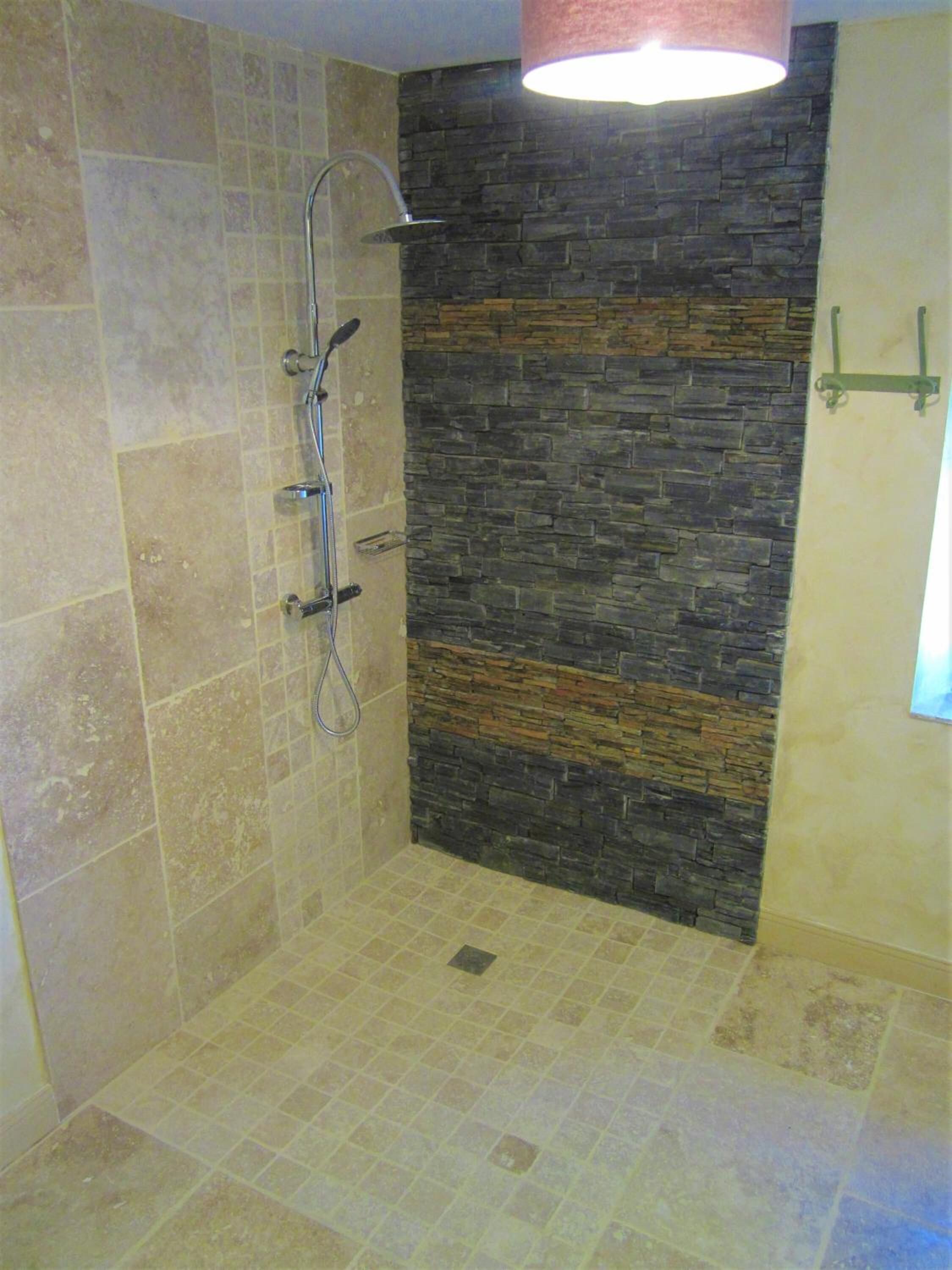 A shower area with a stone wall, a tiled floor, and a hanging light fixture.