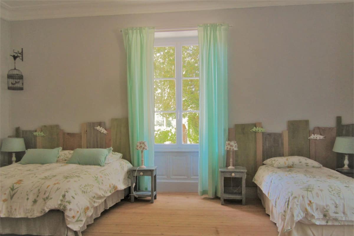 A room with two beds, a window with curtains, and a lamp on each side.