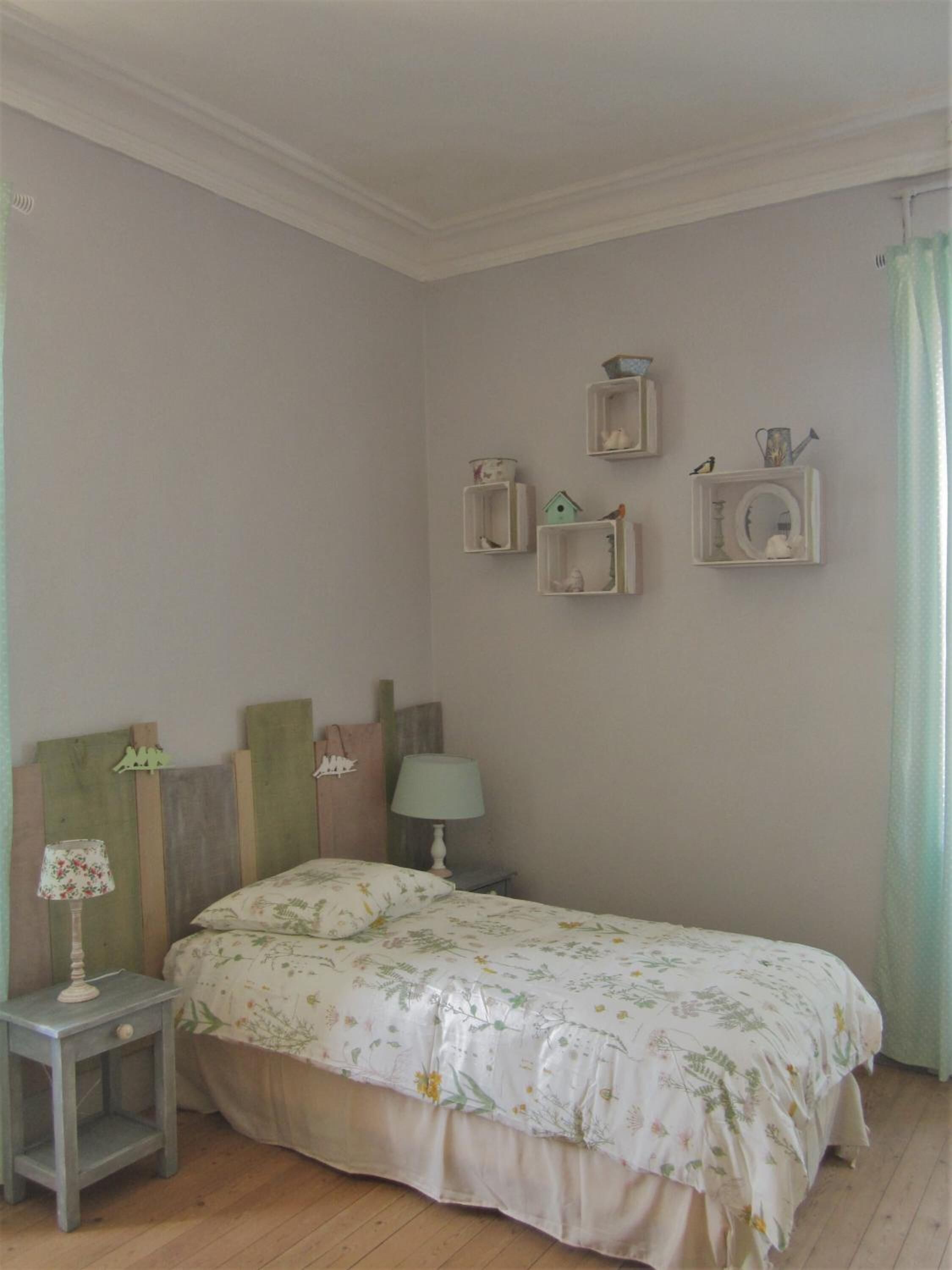 Une chambre à coucher comprenant un lit, une table de chevet, une lampe et des étagères murales décorées d’objets d’ornement.