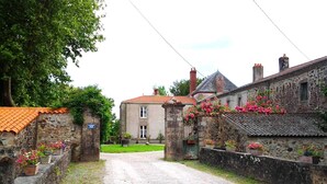 Un bâtiment en pierre avec un toit recouvert de tuiles rouges, une allée gravillonnée et des jardinières le long des murs.