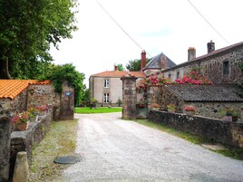 Un edificio de piedra con techo de tejas rojas, camino de grava y jardineras con flores a lo largo de las paredes.