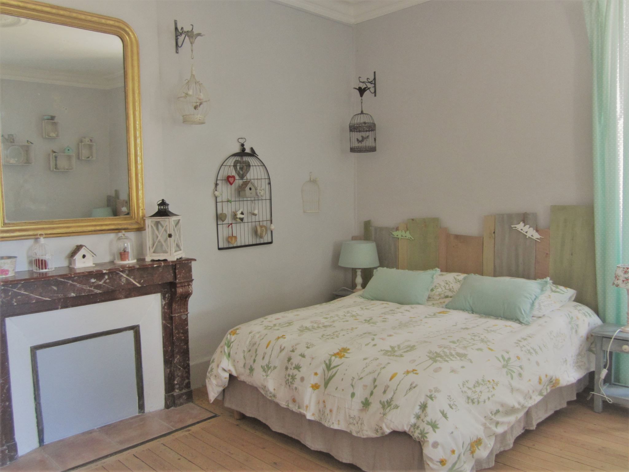 A bedroom with a bed, a dresser, a mirror, and wall decorations including birdcages and a fireplace.
