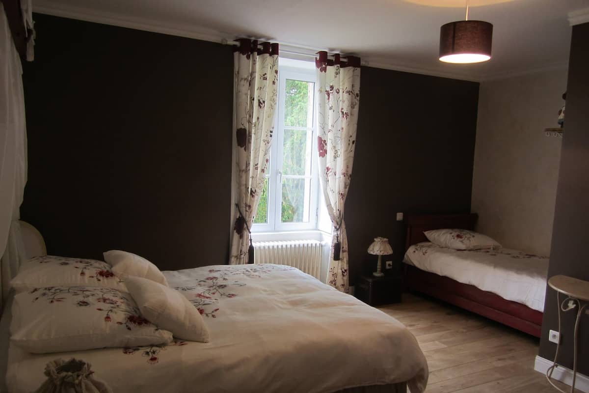 A bedroom with two beds, a window with curtains, a bedside lamp, and a radiator.