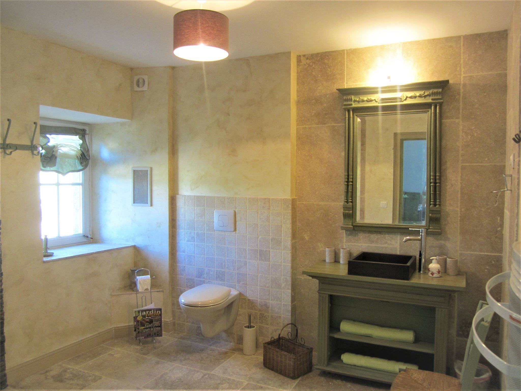 A bathroom with a toilet, sink, mirror, and a window.
