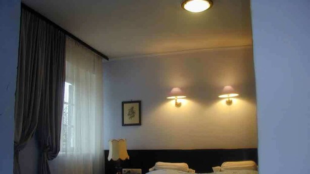 Una habitación de hotel con una cama, una mesita de noche, una lámpara y una luminaria en la pared.