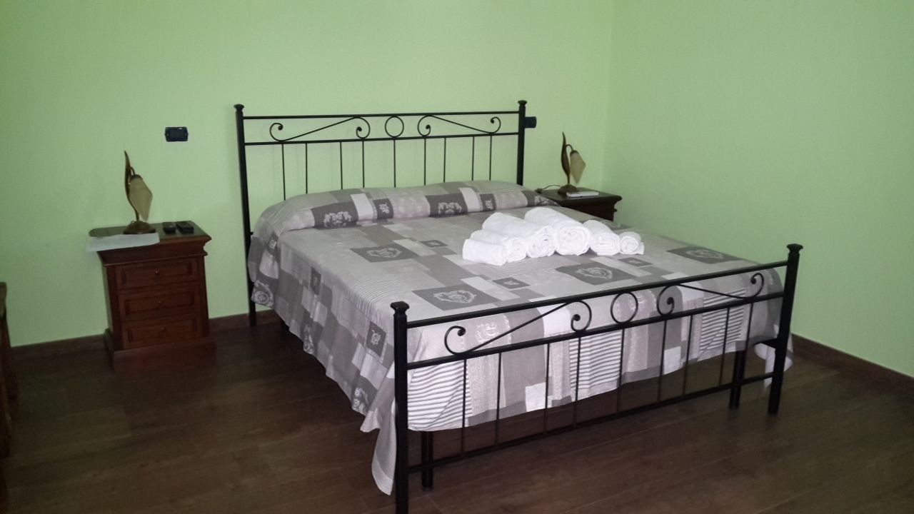 A neatly made bed with a metal frame, a wooden nightstand with a lamp, and a small dresser.