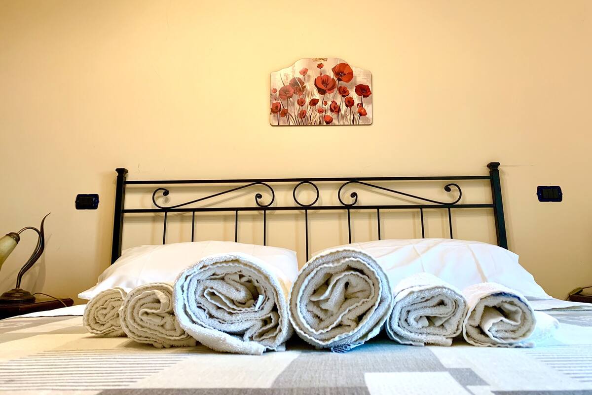 Een netjes opgemaakt bed met opgerolde handdoeken en een kunstwerk erboven.