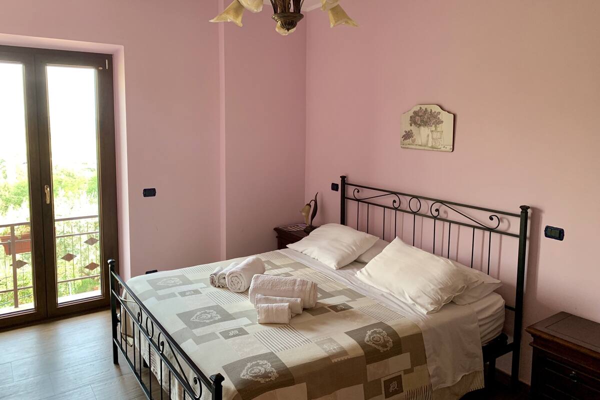 Een slaapkamer met een bed, nachtkastje, een wandlamp en een balkondeur.