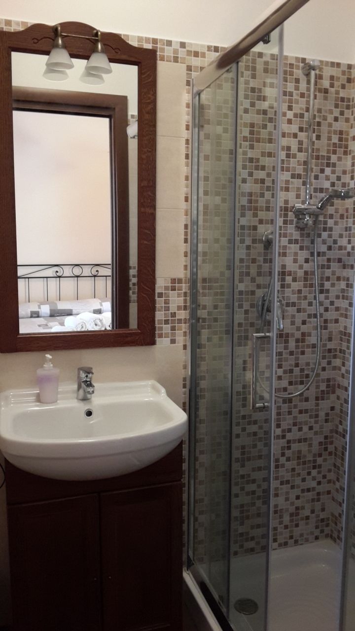 Ein Badezimmer mit einer Duschkabine aus Glas, einem weißen Waschbecken und einem Spiegel mit Holzrahmen.