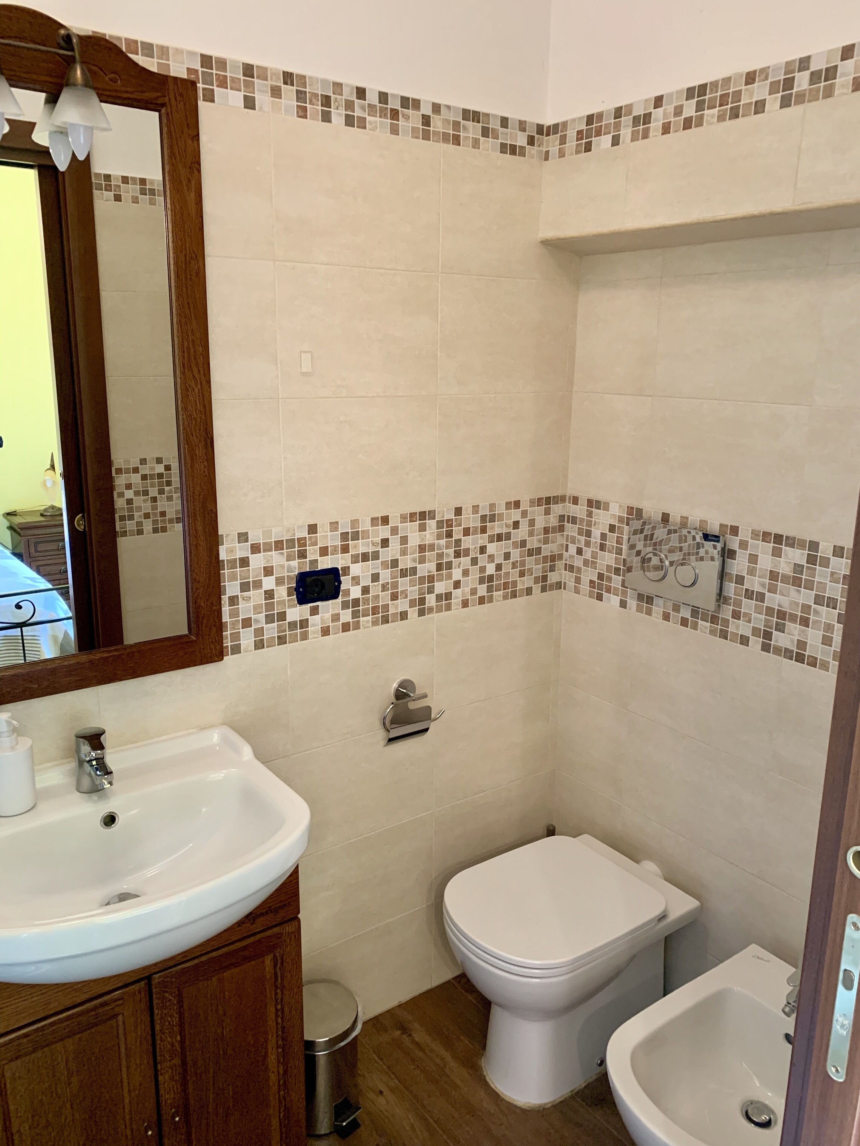 Un baño con lavamanos, inodoro y bidé, paredes con azulejos y un tocador de madera.