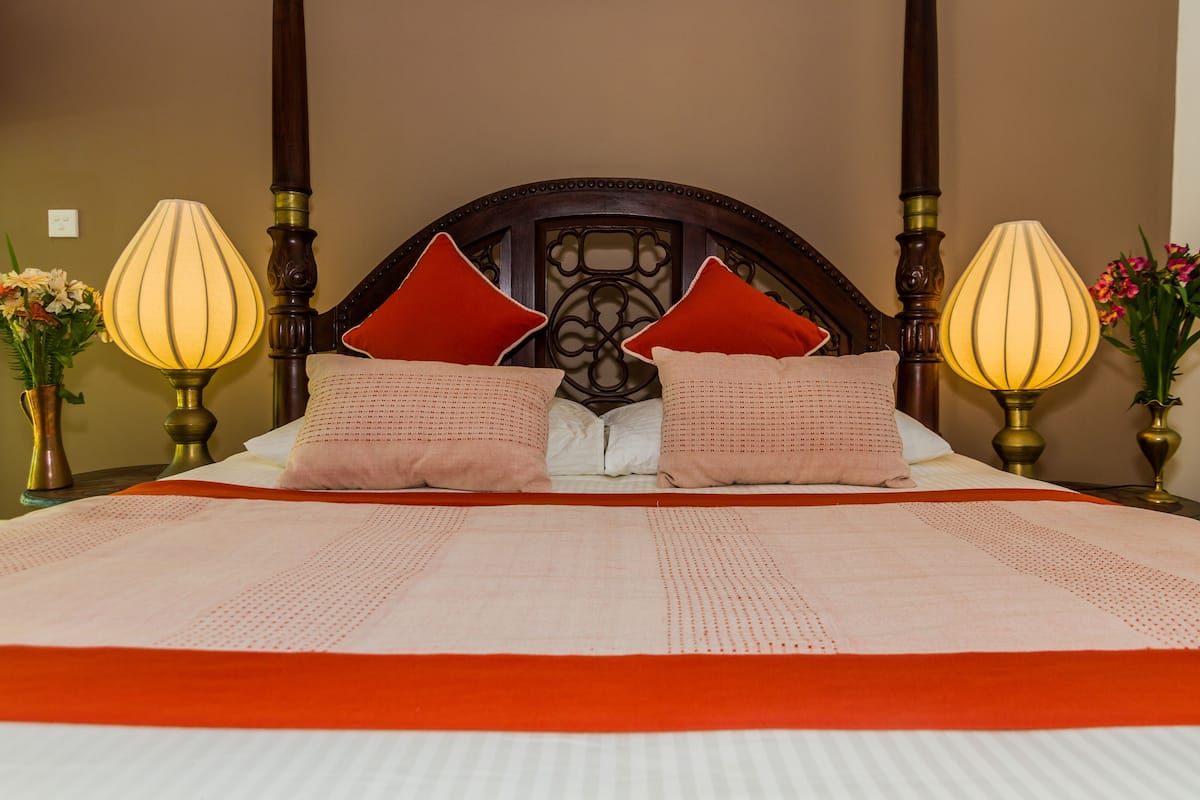 A neatly made bed with a red and white bedspread, two red pillows, and two bedside lamps.