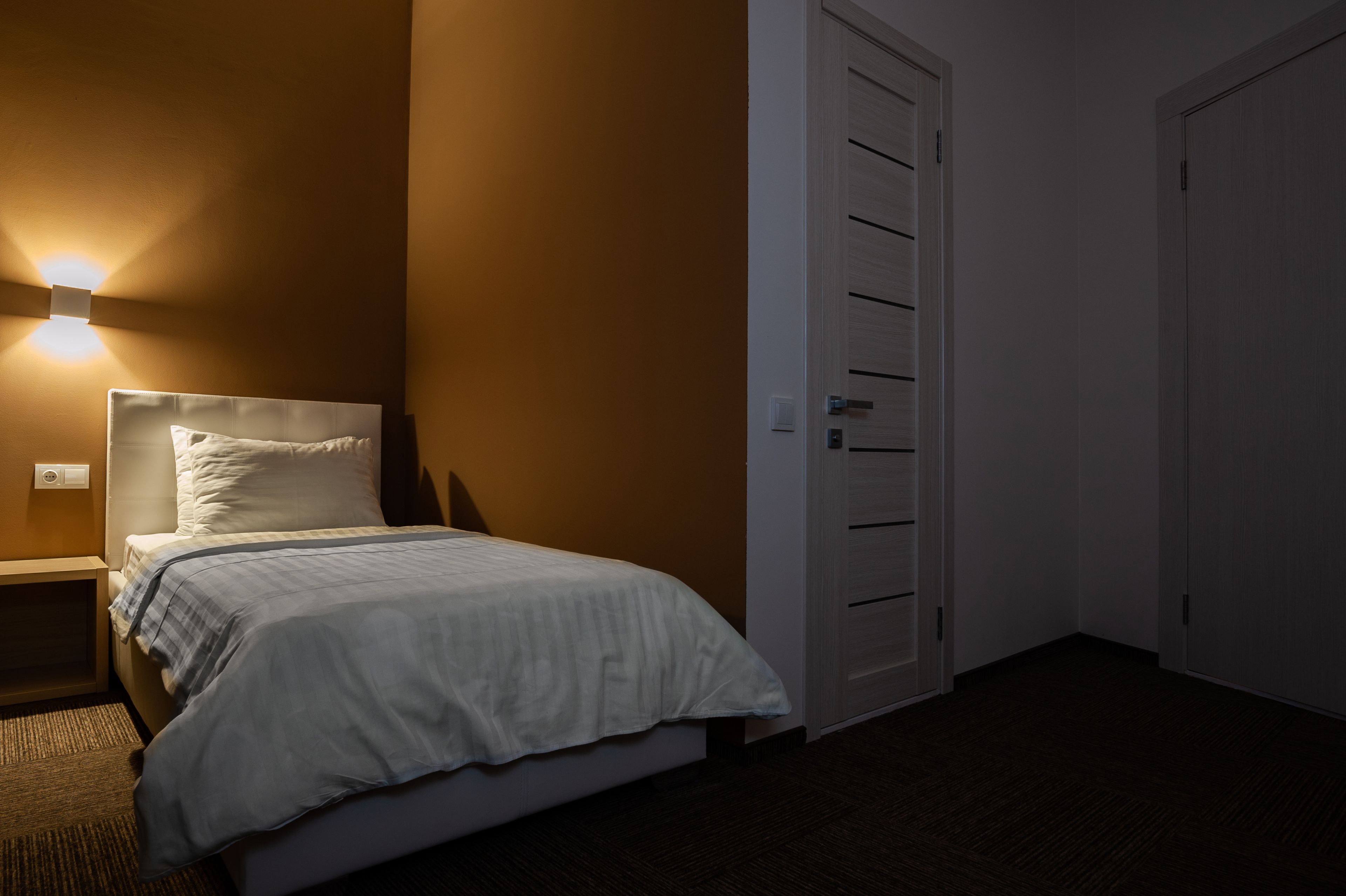 A hotel room with a bed, a nightstand, a wall-mounted light, and a closet with sliding doors.