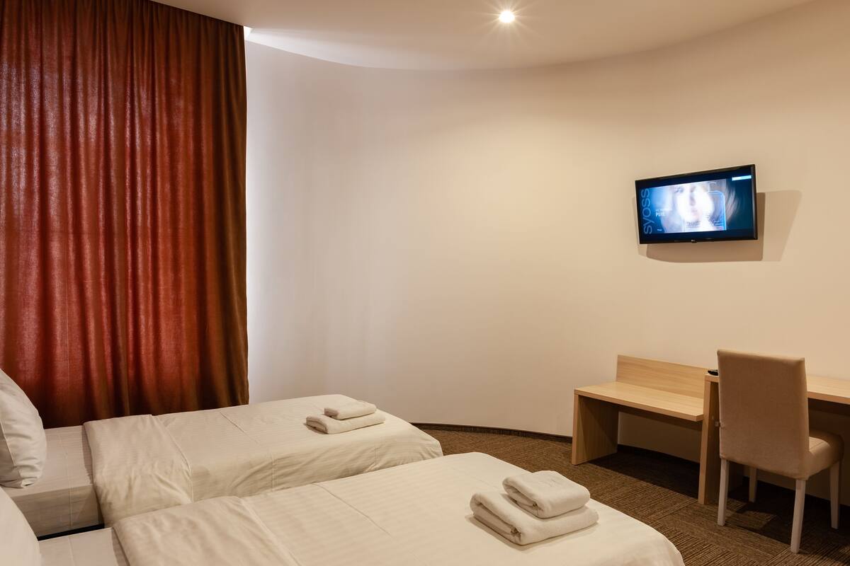 A hotel room with two beds, a desk, a chair, and a TV on the wall.