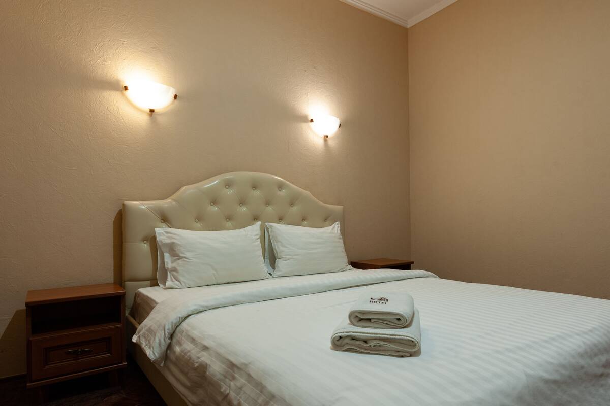 A neatly made bed with a tufted headboard, two bedside tables, and two wall-mounted lights.