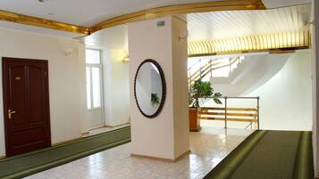 Un pasillo de hotel con una puerta de madera, un espejo, una escalera y una planta.