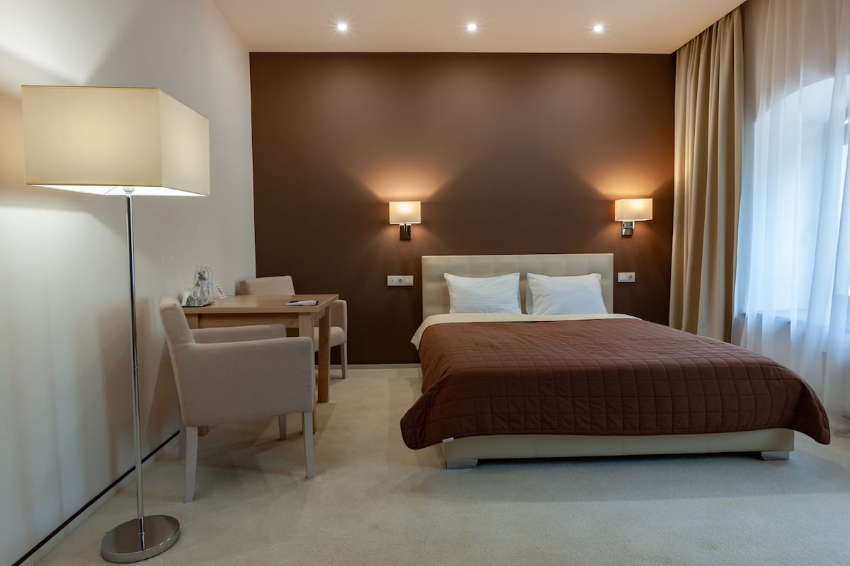 A hotel room with a bed, two bedside lamps, a desk with a chair, and a floor lamp.