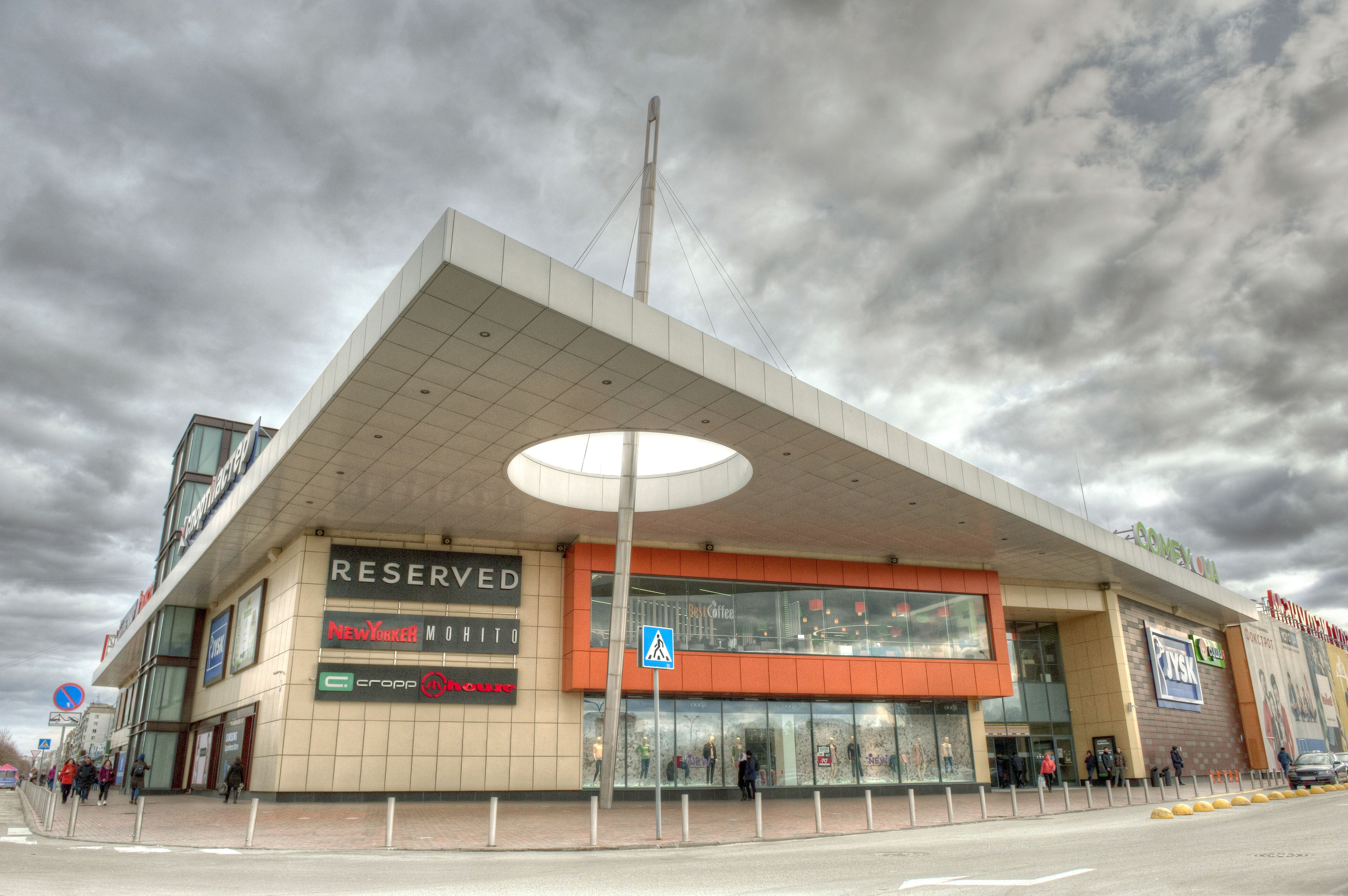 A modern building with a large overhang, a pedestrian crossing sign, and multiple storefronts including a coffee shop.