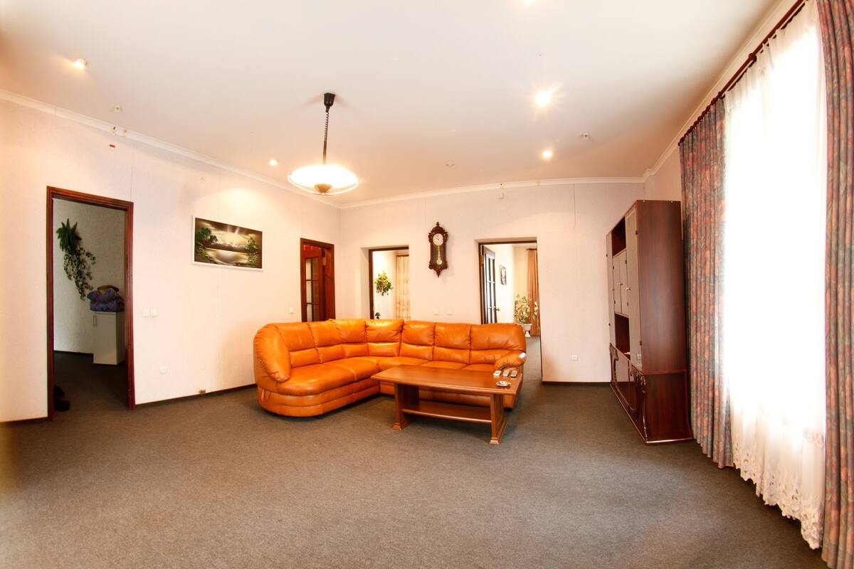 A living room with a large L-shaped orange leather sofa, a wooden coffee table, and a ceiling light fixture.