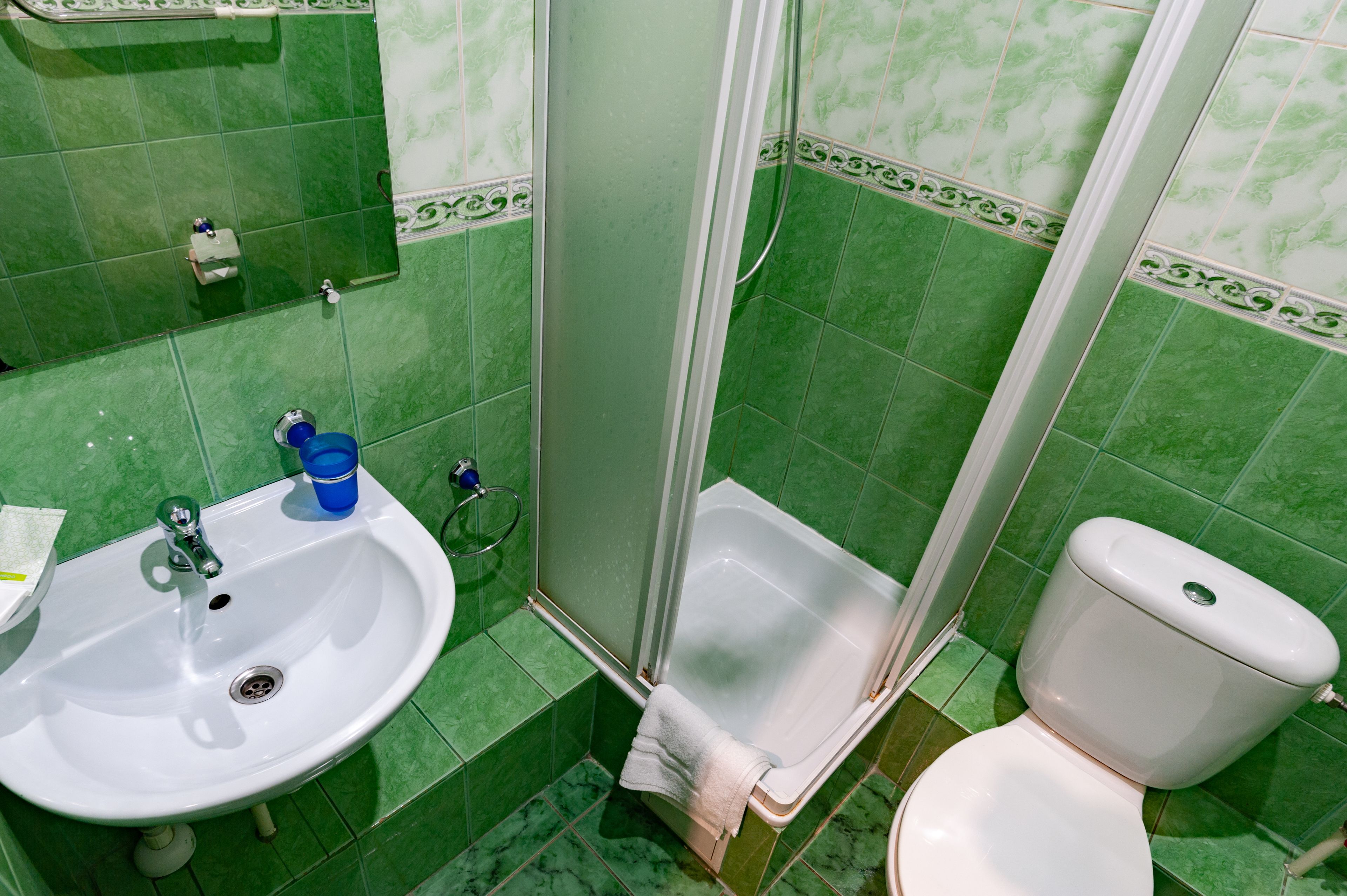 A bathroom with green tiles, a white sink, a toilet, and a shower enclosure.
