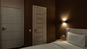 A hotel room with a bed, a nightstand, a wall-mounted light, and a door.