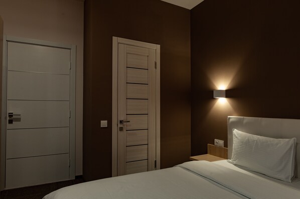 A hotel room with a bed, a nightstand, a wall-mounted light, and a door.