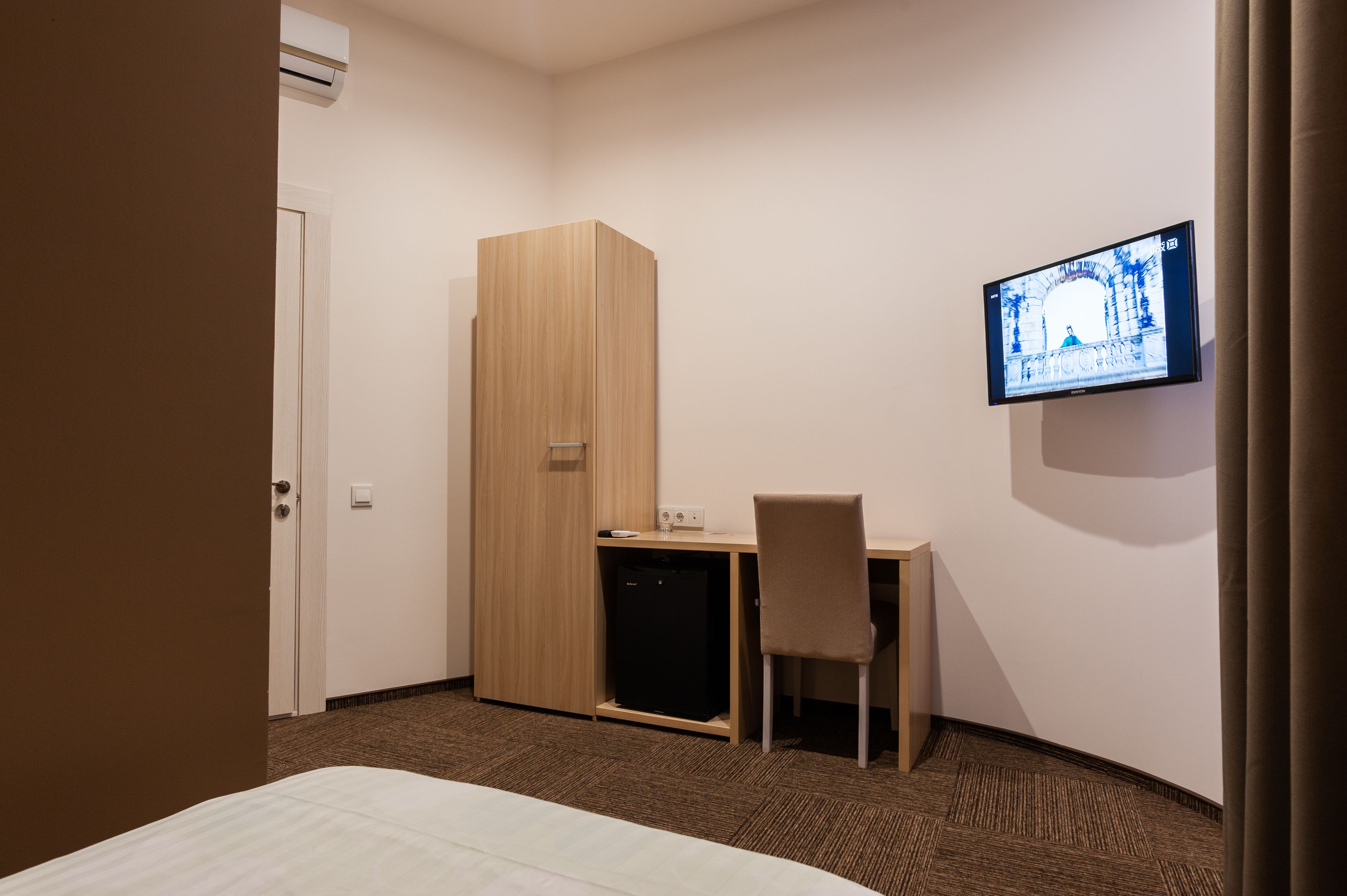 Una habitación de hotel con cama, escritorio, silla, armario, televisor y un refrigerador pequeño.