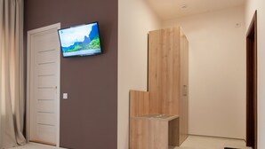A room with a television mounted on the wall, a wooden wardrobe, and a door with a sliding mirror.