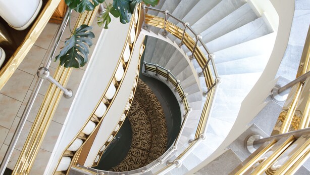 A spiral staircase with a gold railing, white steps, and a patterned carpet.