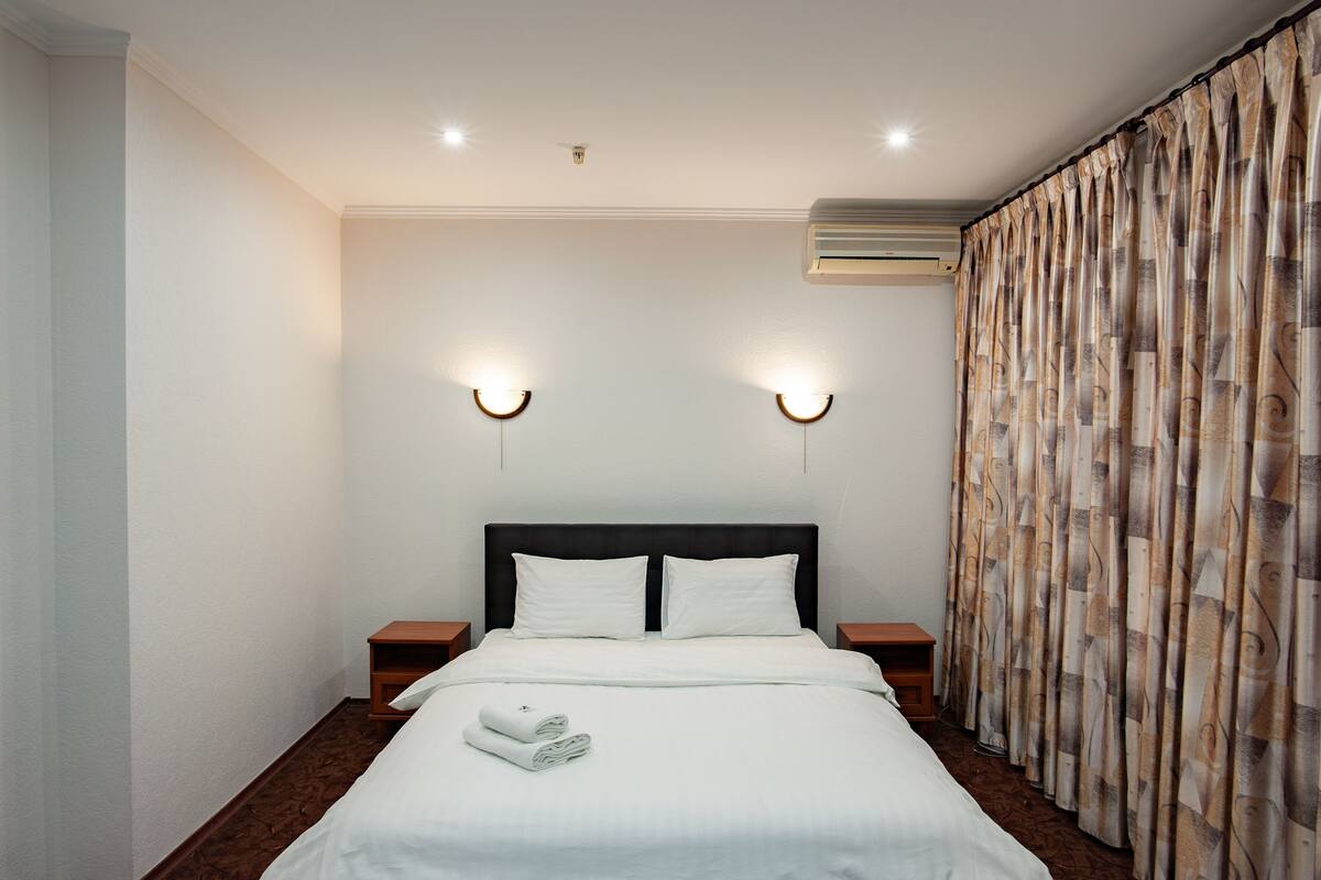 A hotel room with a neatly made bed, two bedside tables, and a large window with curtains.