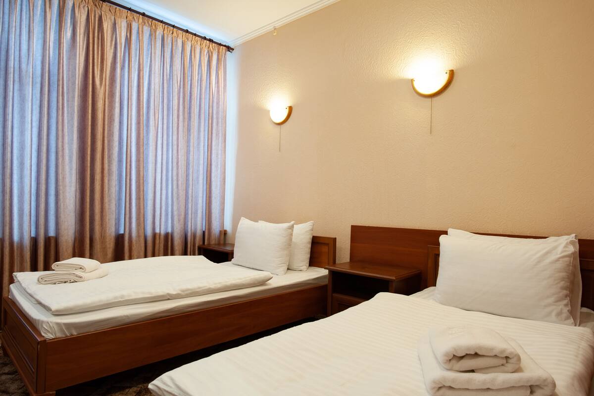A hotel room with two beds, a wooden headboard, a nightstand, and a wall-mounted light fixture.