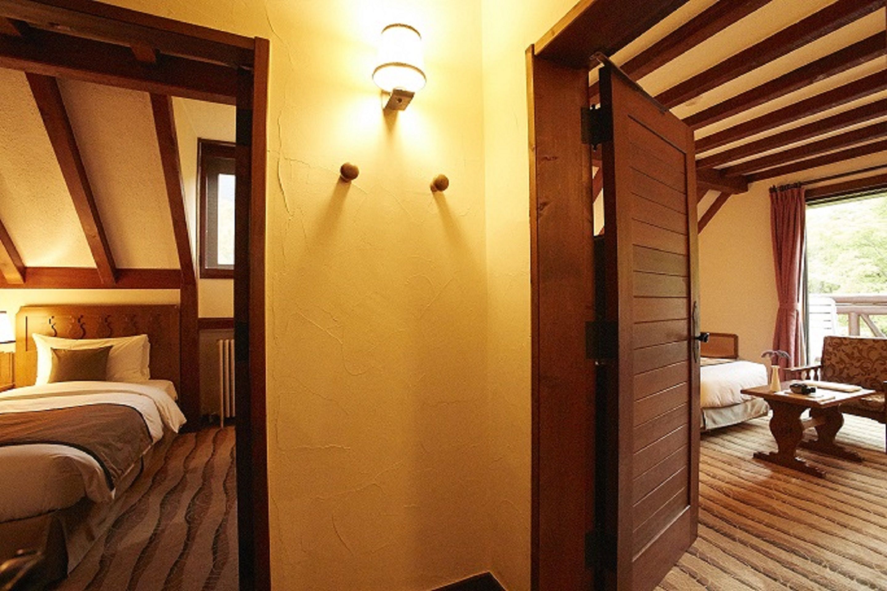 A hotel room with a wooden ceiling, a bed with a headboard, a bedside table, and a window with curtains.