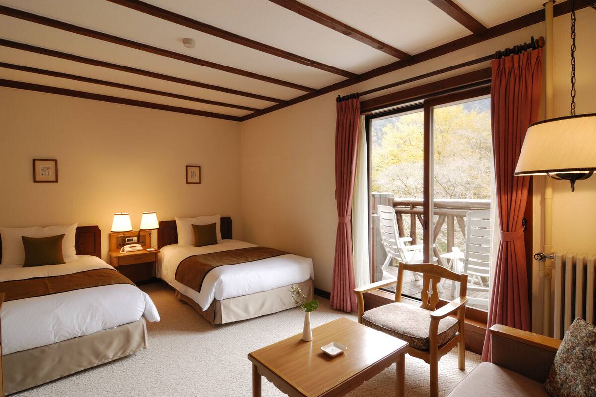 Een hotelkamer met twee bedden, een houten tafel, een stoel en uitzicht op de omgeving.