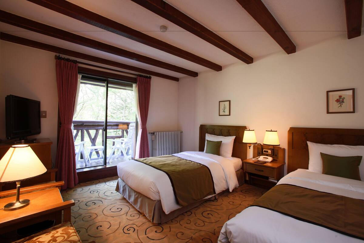 Een hotelkamer met twee bedden, een televisie, een bureau met lamp en een raam met gordijnen.