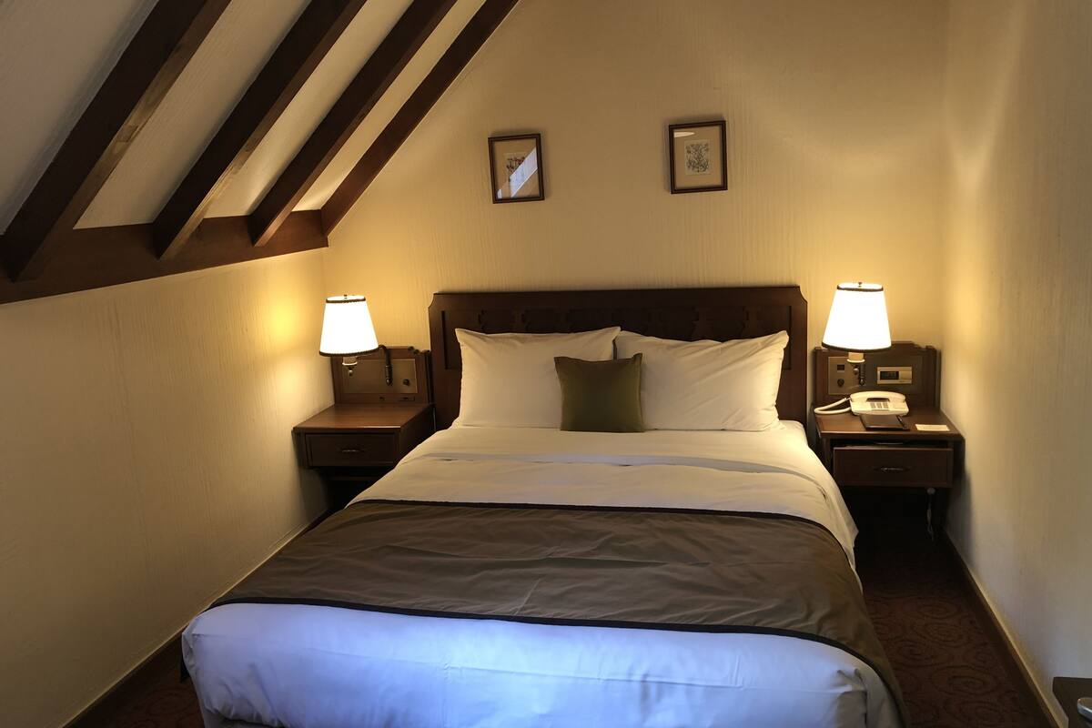 Een hotelkamer met een groot bed, twee nachtkastjes met lampen, een houten hoofdeinde en twee ingelijste foto's aan de muur.
