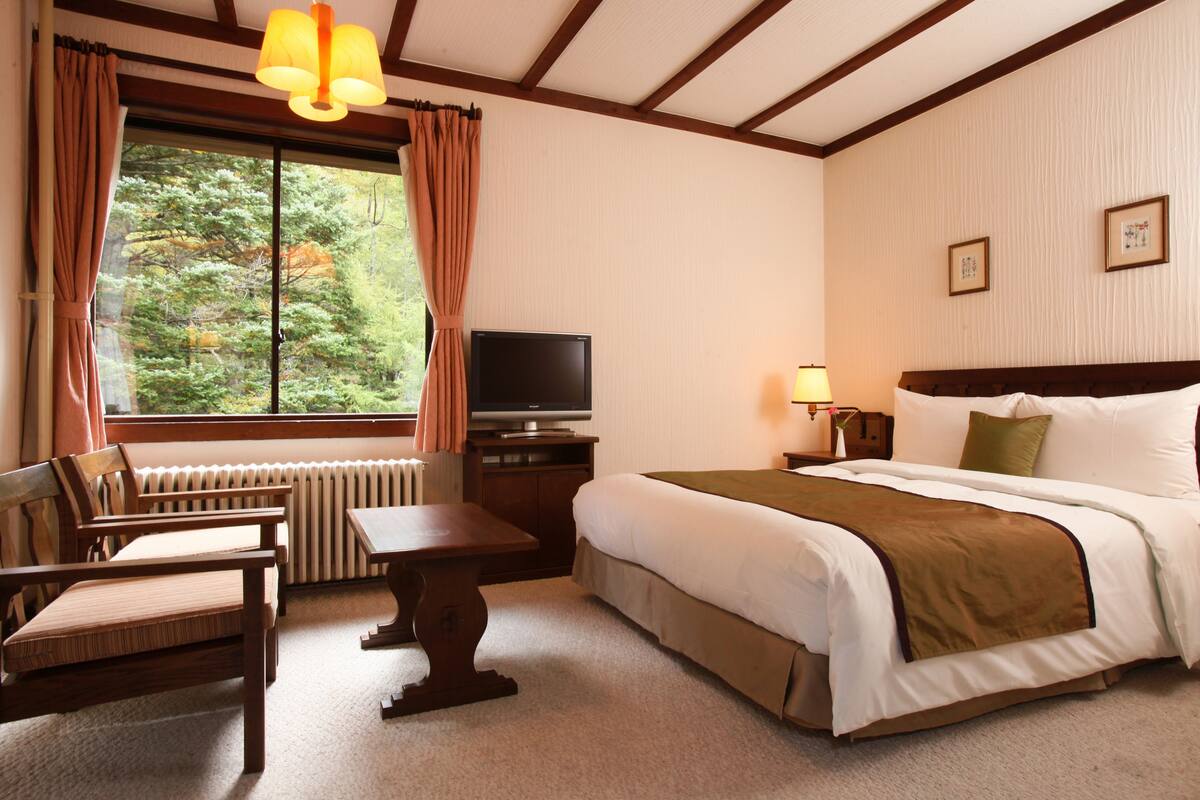 Hotelkamer met een bed, een bureau, een stoel, een televisie en een raam met gordijnen.