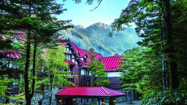 Un chalet au toit rouge, niché au cœur d’une forêt et entouré de montagnes.