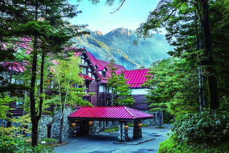 A lodge with a red roof nestled in a forest, surrounded by mountains.