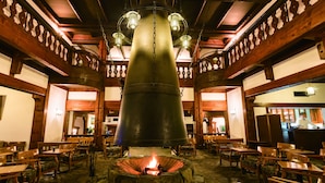 Une cheminée en pierre avec un feu de bois, des bancs en bois et des tables disposées autour, créant une ambiance rustique.