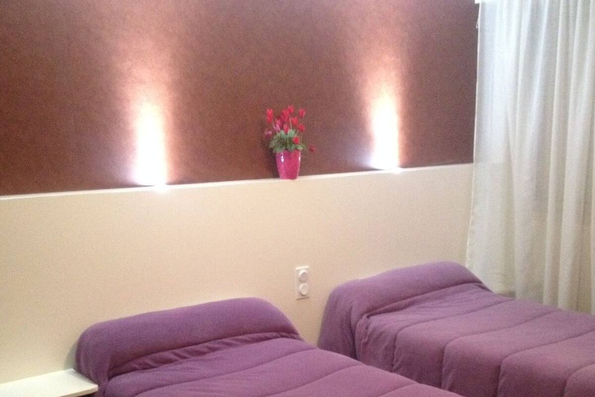 Een hotelkamer met twee bedden, een klein raam, een wandlamp en een kamerplant.