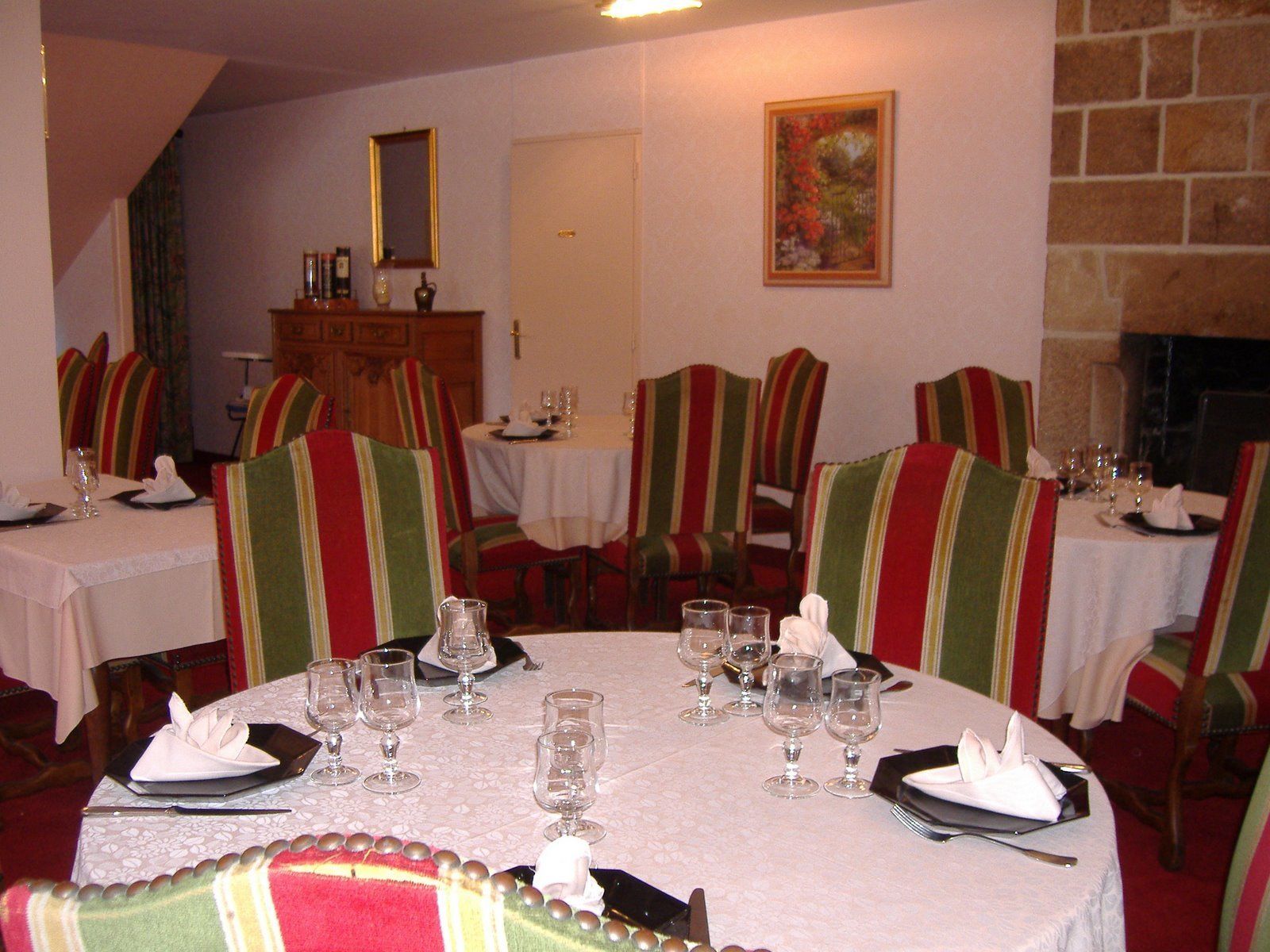 A dining room with round tables, striped chairs, and a fireplace.