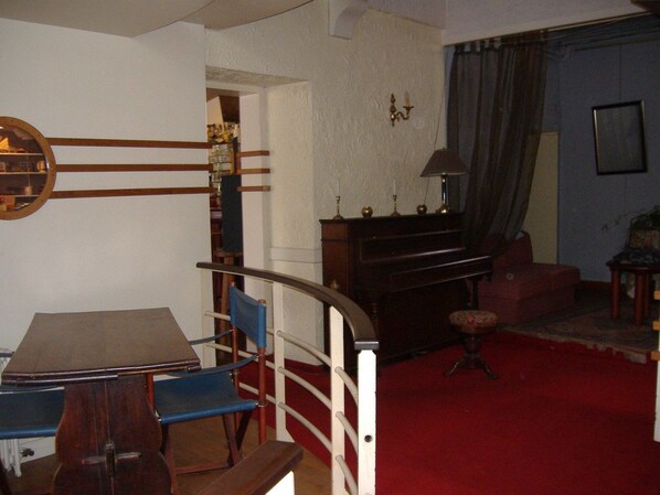 A dining area with a table and chairs, a piano, a red carpet, and a doorway leading to another room.